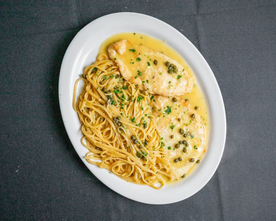Chicken piccata with capers and parsley, served with linguine pasta on a white oval plate.