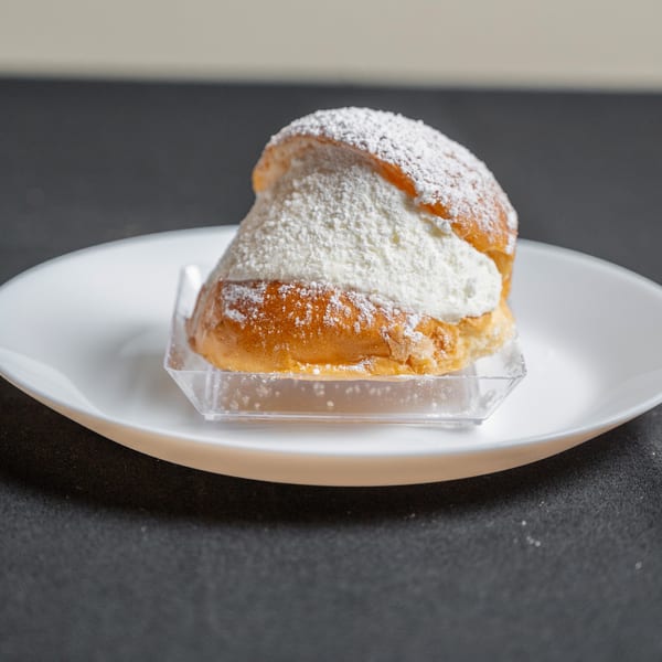 A golden-brown pastry bun, generously filled with white cream and dusted with powdered sugar, on a white plate.