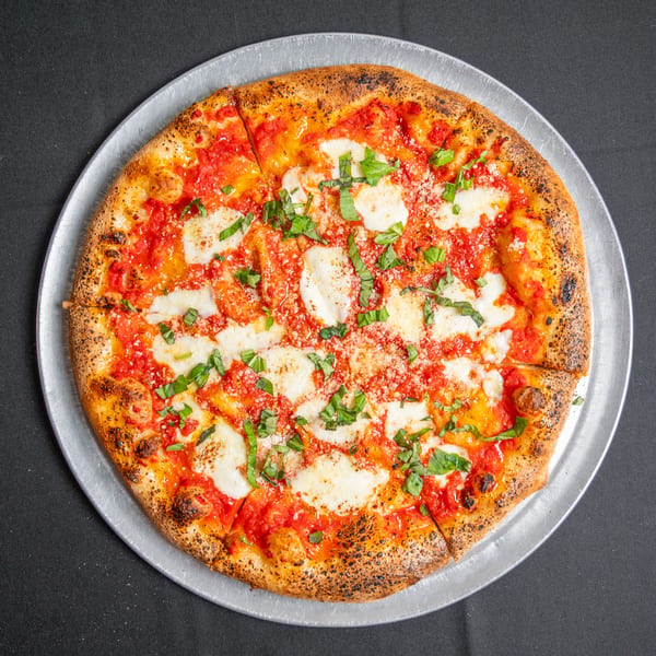A whole Margherita pizza with fresh mozzarella, tomato sauce, and basil on a metal tray.