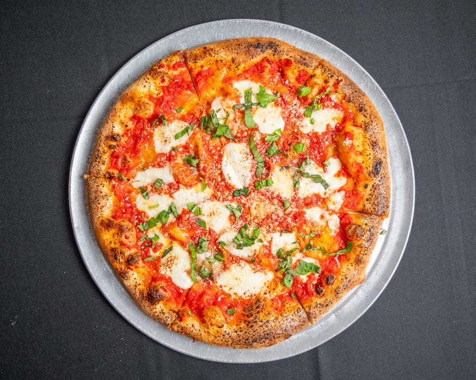 A whole Margherita pizza with fresh mozzarella, tomato sauce, and basil on a metal tray.