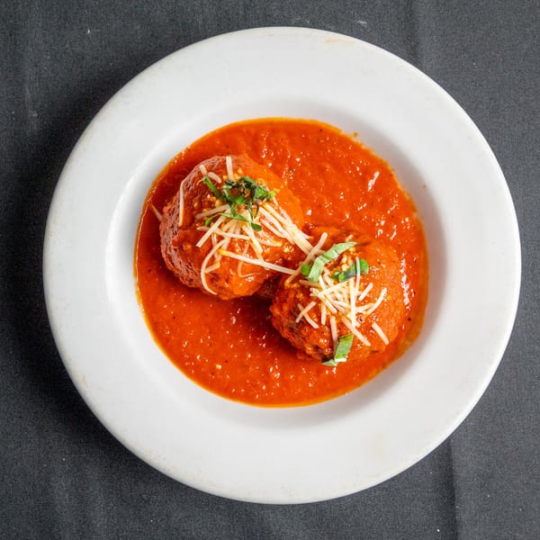 Two meatballs in rich red tomato sauce, topped with shredded cheese and fresh basil, on a white plate.