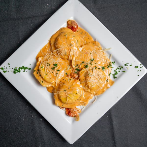 Ravioli in a creamy orange sauce, topped with shredded cheese and parsley, on a white plate.