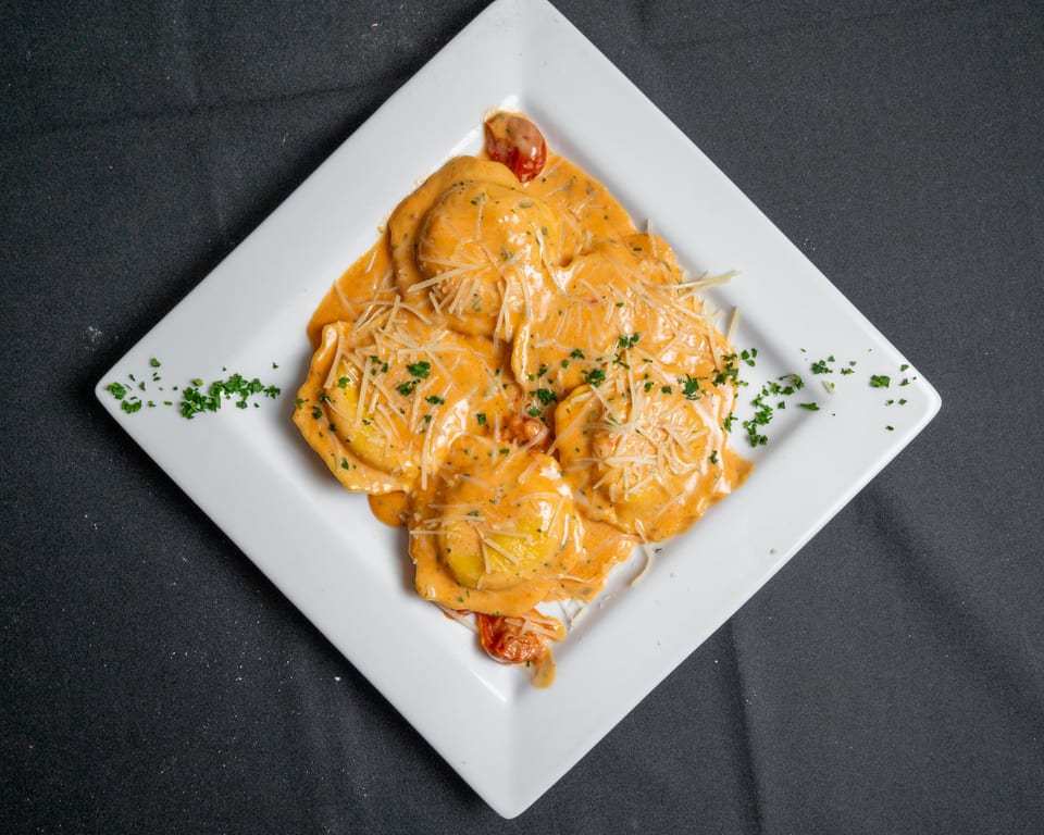 Ravioli in a creamy orange sauce, topped with shredded cheese and parsley, on a white plate.
