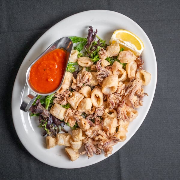 Fried calamari with marinara sauce, a lemon wedge, and mixed greens on a white platter.