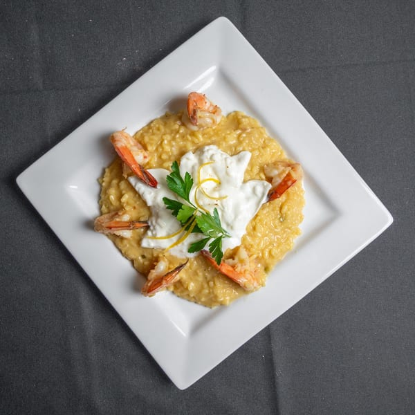 Creamy risotto with shrimp, a dollop of white sauce, lemon zest, and parsley on a white plate.