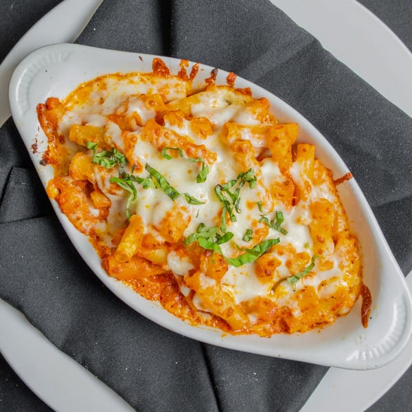 Baked ziti pasta with melted cheese and fresh basil in a white dish on a black napkin.