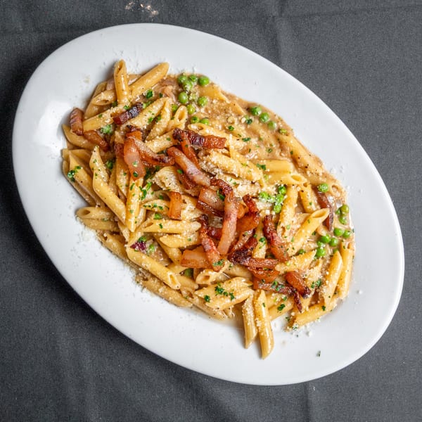 Penne pasta with crispy bacon, green peas, and parmesan cheese in a creamy sauce.