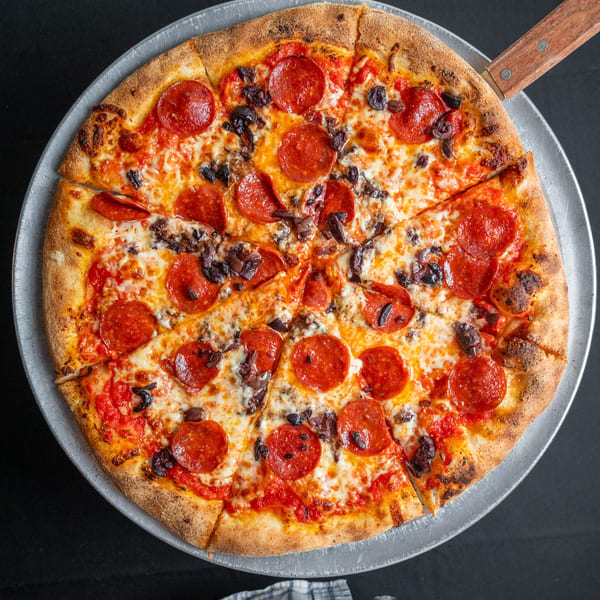 A whole pepperoni and olive pizza, sliced into eight pieces, on a metal pizza pan.