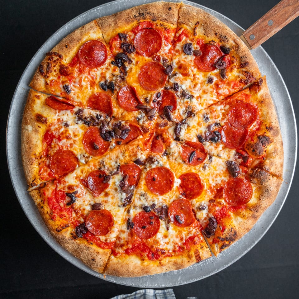 A whole pepperoni and olive pizza, sliced into eight pieces, on a metal pizza pan.