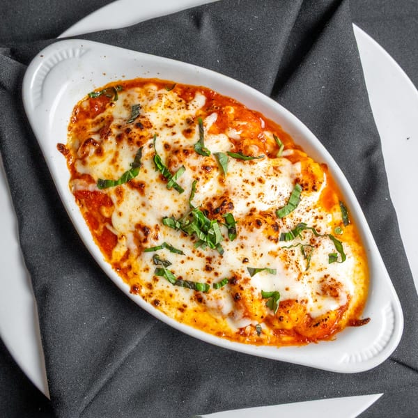 Baked gnocchi in tomato sauce with melted mozzarella cheese and fresh basil in a white dish.