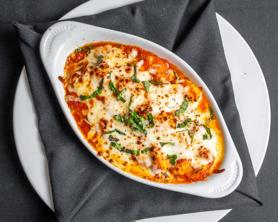 Baked gnocchi in tomato sauce with melted mozzarella cheese and fresh basil in a white dish.