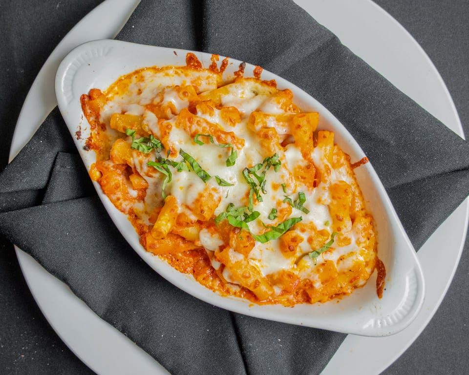 Baked ziti pasta with melted cheese and fresh basil in a white dish on a black napkin.