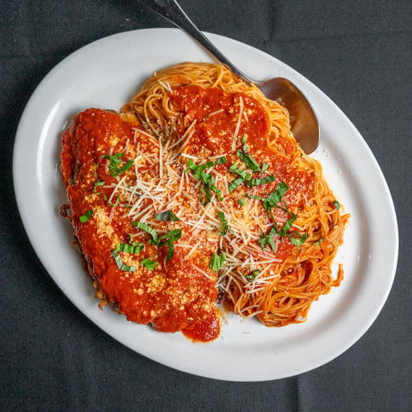 Chicken parmesan with spaghetti, red sauce, cheese, and basil on a white plate with a spoon.