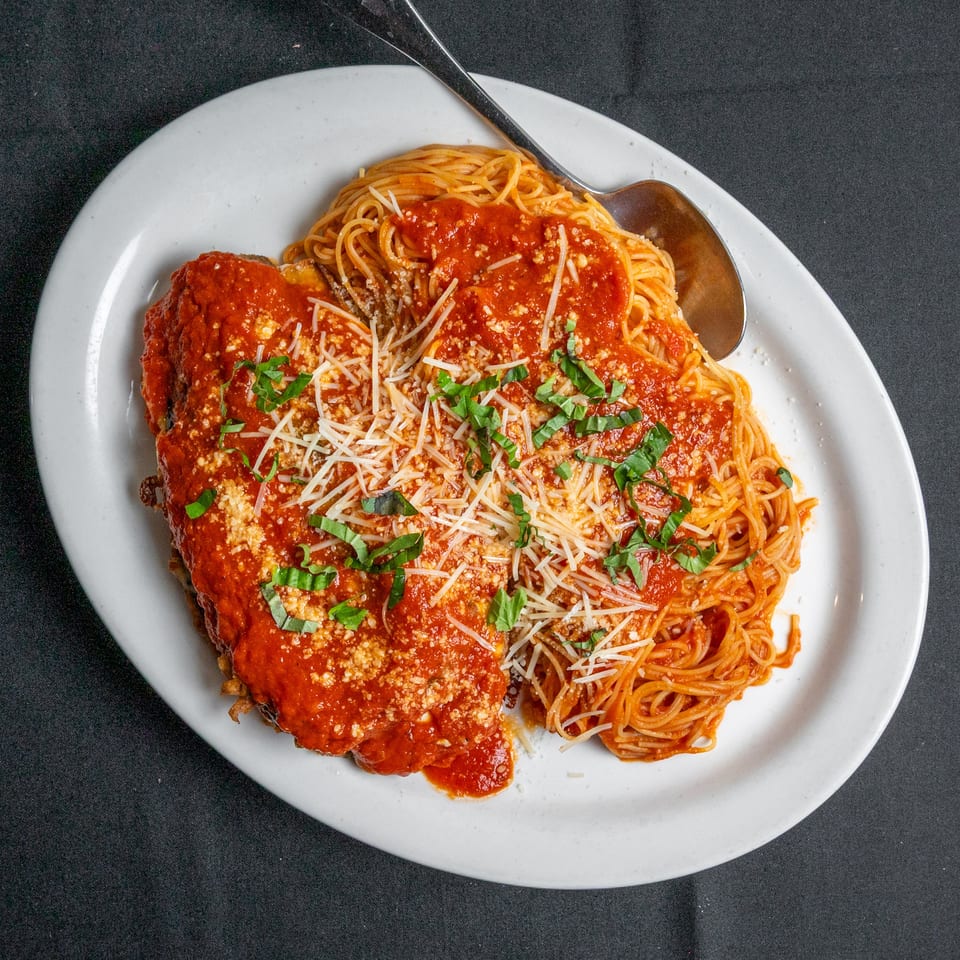Chicken parmesan with spaghetti, red sauce, cheese, and basil on a white plate with a spoon.