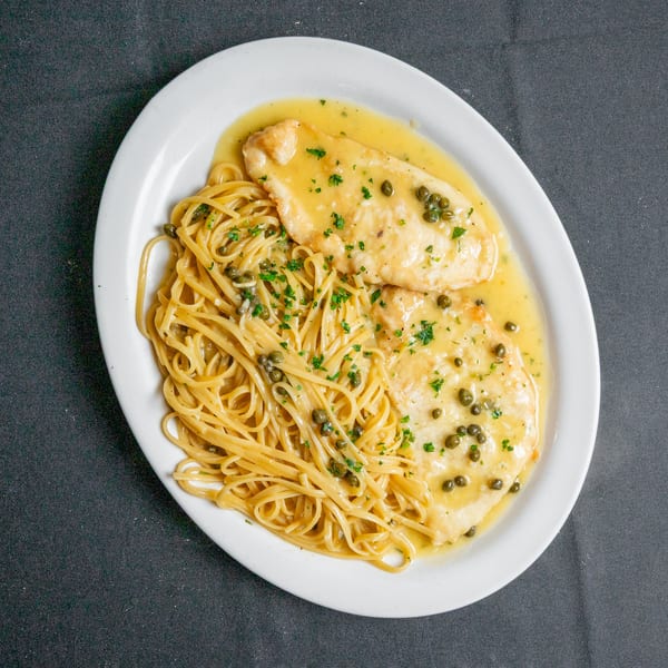 Chicken piccata with capers and parsley, served alongside linguine pasta on a white oval plate.