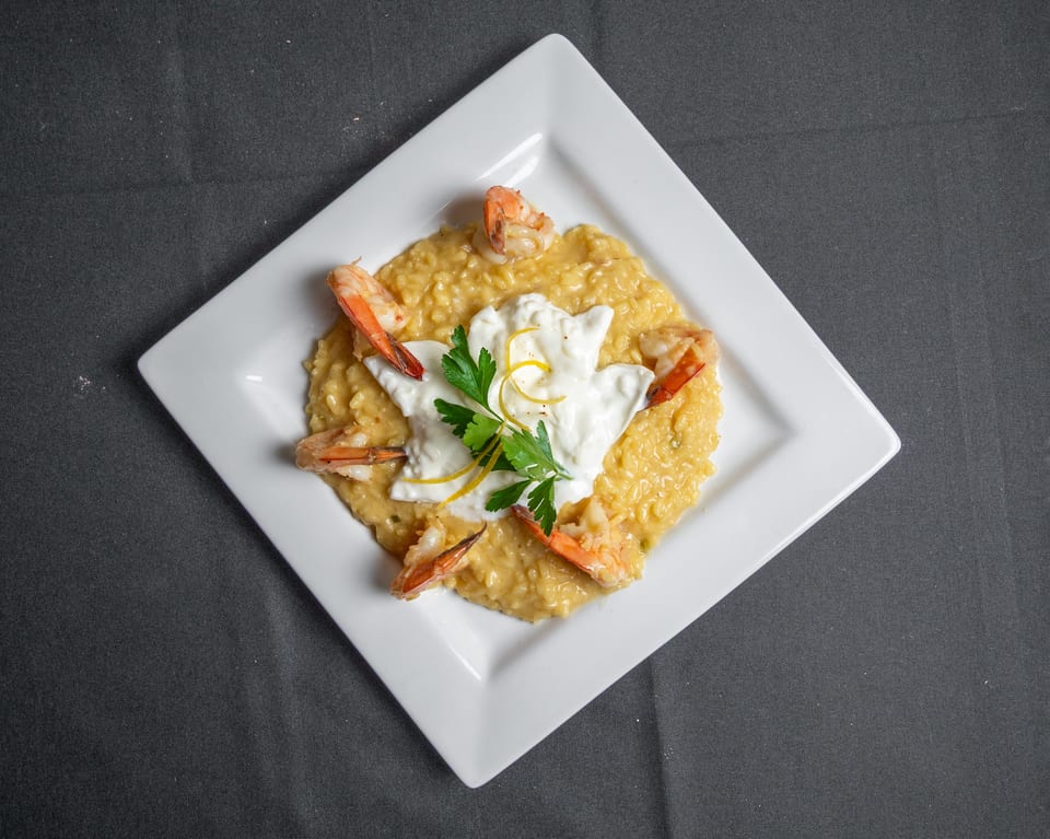 Creamy risotto with shrimp, a dollop of white sauce, lemon zest, and parsley on a white plate.